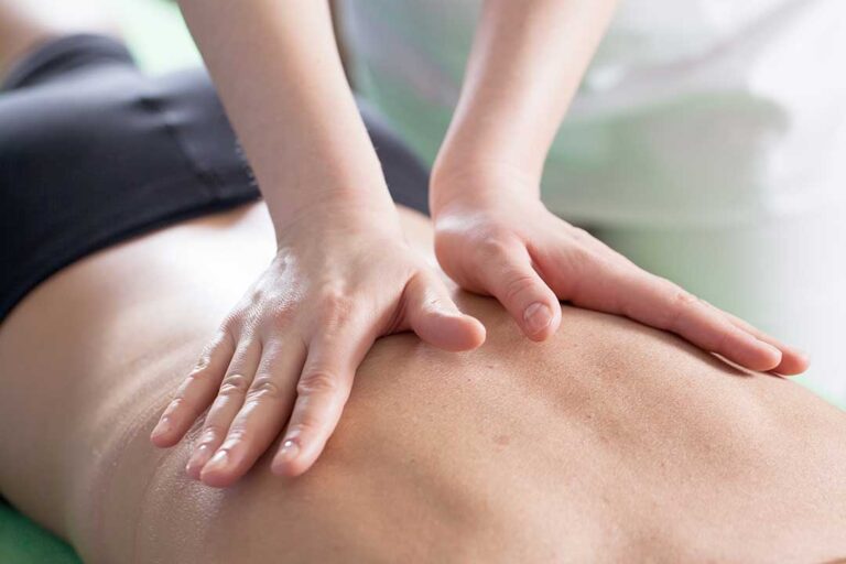A chiropractor examines a patient's spine while the patient sits on an exam table.